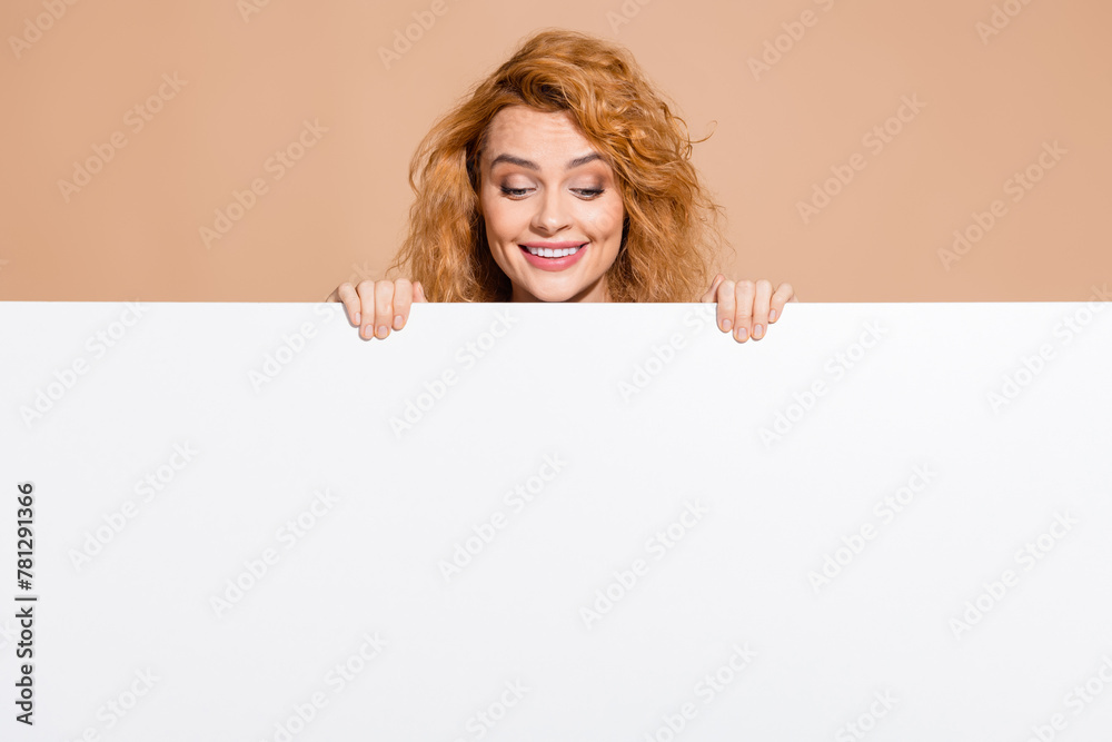 Photo portrait of lovely young lady hide behind look white empty space dressed stylish striped garment isolated on beige color background Photo portrait of lovely young lady hide behind look white empty space dressed stylish striped garment isolated on beige color background