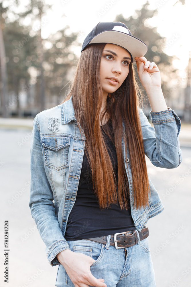 beautiful youth young girl in denim clothes with a jacket and jeans wears a cap and walks in the park at sunset beautiful youth young girl in denim clothes with a jacket and jeans wears a cap and walks in the park at sunset