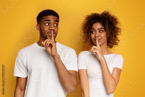 Amazed black couple make silence sign, keep forefingers on lips photo