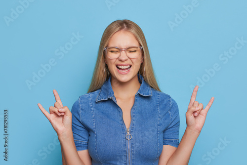 Wearing glasses, smiling, making rock and roll sign with hand