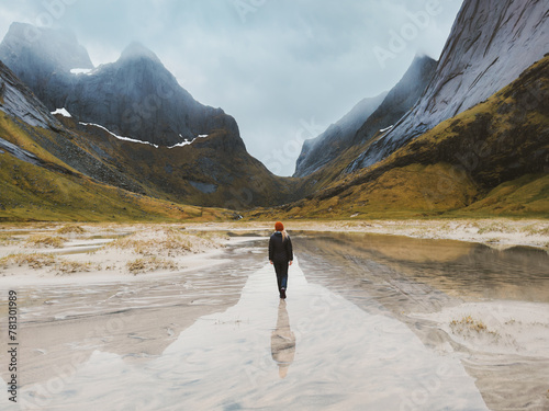 Traveler woman walking alone on flooded Horseid beach sandy dunes in Norway travel lifestyle summer vacations in Lofoten islands outdoor mountains water reflection, eco tourism