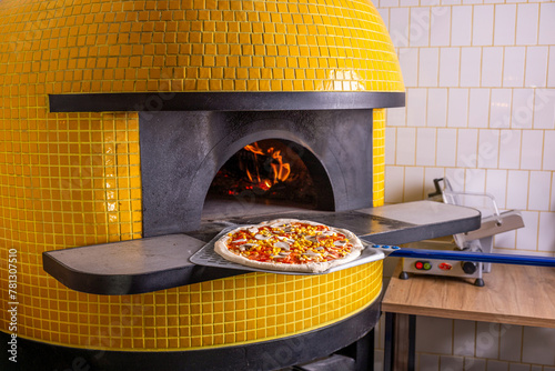 Baked tasty pizza in raditional wood oven in restaurant, Italy. Red hot coal. Italian pizza is cooked in a wood-fired oven. hef holding shovel for pizza, photo