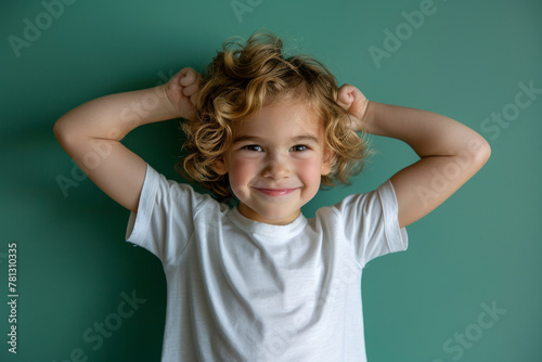 A happy and healthy young boy is standing and flexing his arms muscle on green background.