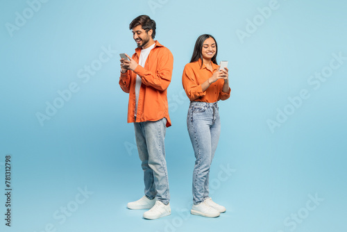 Couple using smartphones back to back on blue background © Prostock-studio