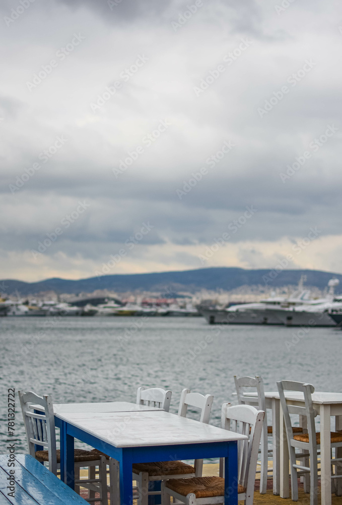Fototapeta premium Experience authentic Greek cuisine by the marina, surrounded by luxury yachts under a cloudy sky.