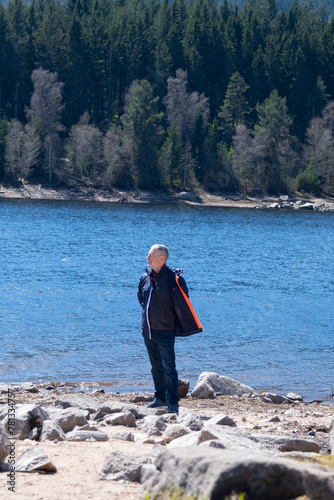 A senior man in jacket is staying on the bank near the blue lake