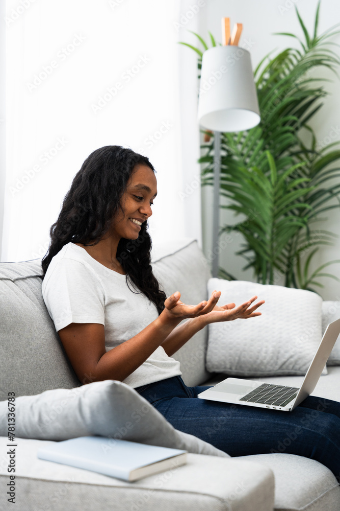 Young Indian woman talking on laptop sitting on sofa. Young Indian woman talking on laptop sitting on sofa.
