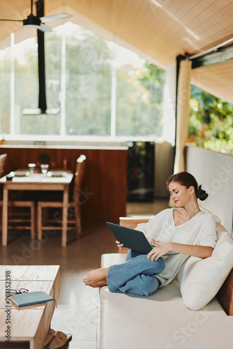 Relaxed woman browsing online shopping on her laptop while sitting on a cozy modern sofa in her comfortable living room Her smiling face reflects the joy of finding great deals as she enjoys her