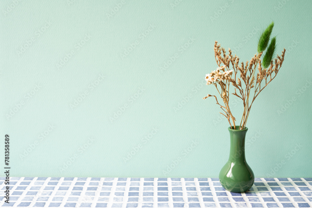 Green vase of dry flower on blue tile table. mint wall background
