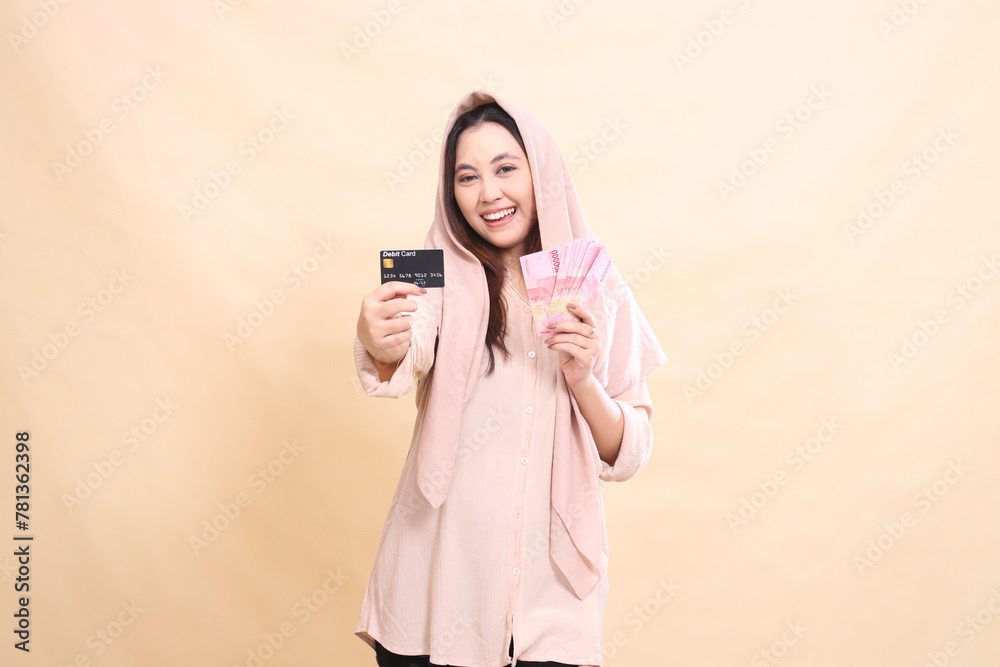 Asian woman with smiling expression laughing at you, holding your debit card in front of you and carrying rupiah money. young beautiful for finance, advertising, fashion Asian woman with smiling expression laughing at you, holding your debit card in front of you and carrying rupiah money. young beautiful for finance, advertising, fashion