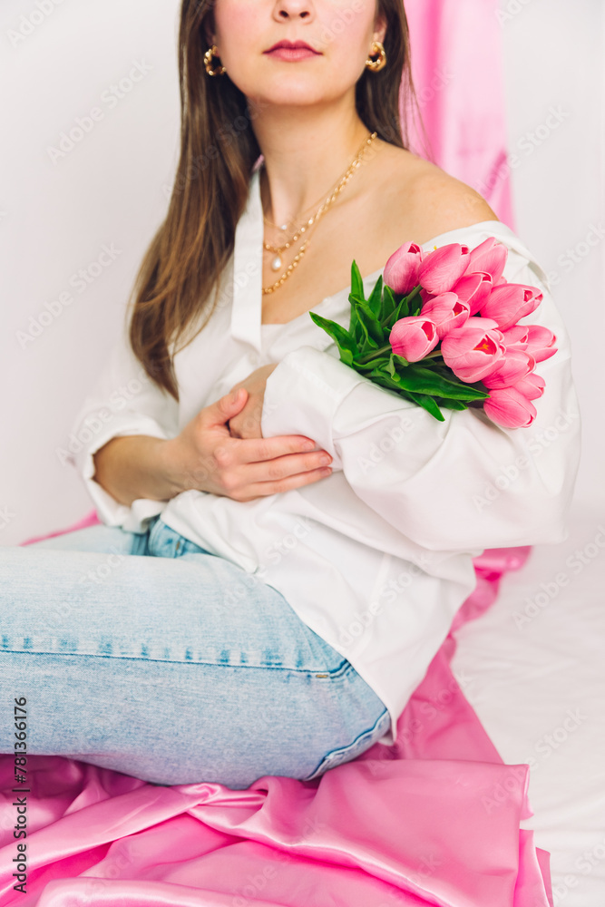 Faceless woman holding pink tulips in her arms. Gold jewelry and casual attire. Spring vibes, modern, classy, chic, trendy. 