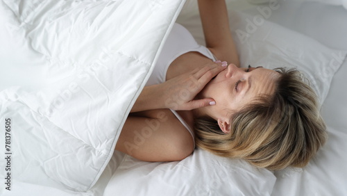 Woman looks in shock under covers in bed. Bedwetting in women concept photo