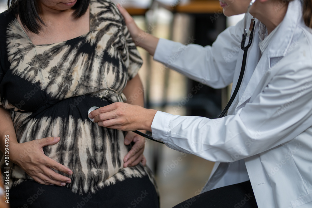 A doctor consults a pregnant patient, taking notes while discussing her symptoms and well-being during a prenatal visit.