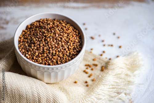 Bowl full of organic raw buckwheat on wooden table with towel photo