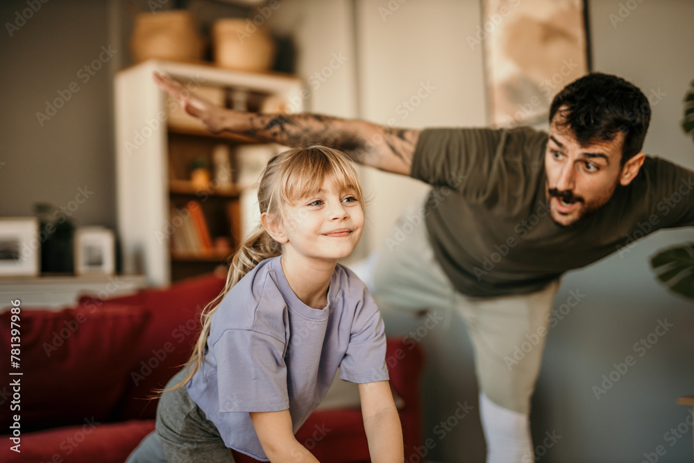 A little girl and her father during a home workout learning how to balance - obrazy, fototapety, plakaty 