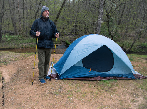 Senior hiker in cold weather with hiking poles standing by his tent. © charles eberson