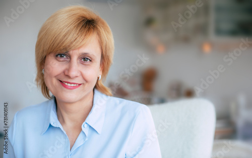 Close-up portrait of smiling mid-aged woman in home interior. Lovely mature caucasian female looking on camera, resting, serene and calm female spending weekend at home