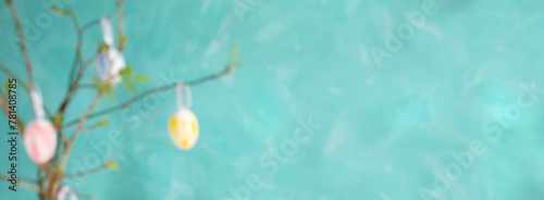 Blurred Easter banner with eggs hanging on spring twigs with young leaves on turquoise. Copy space. © SeNata