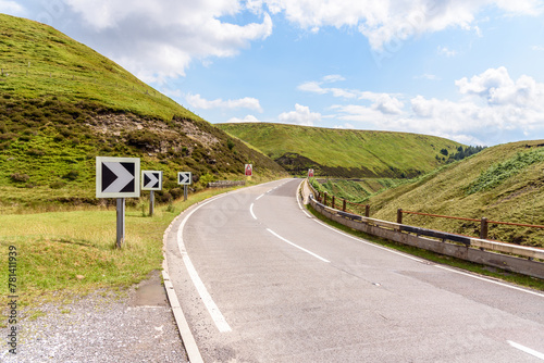 Chevron road signs on a sharp bend along a winding mountain pass road in England on a partly cloudy summer day