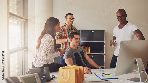 Focused diverse entrepreneurial team standing together around a computer screen they are all looking at. A man points at the screen to show the group something