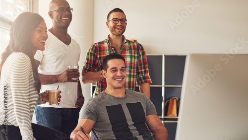 Man showing something on his computer to his three diverse colleagues. They laughing at each other and are happy about what they see on the screen