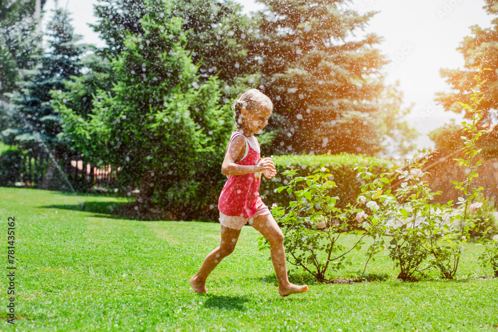 Having fun with Water Garden Sprinklers in Beautiful Garden with Flowers and Sunlight. Child Running Barefoot on Green Nature Background. Happy Children Summer Holidays. Having fun with Water Garden Sprinklers in Beautiful Garden with Flowers and Sunlight. Child Running Barefoot on Green Nature Background. Happy Children Summer Holidays.