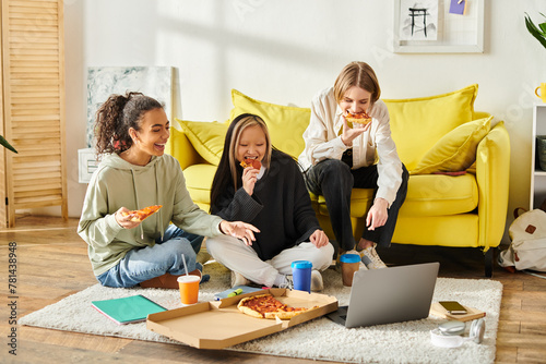 Three young women, representing diversity, sit on the floor enjoying slices of pizza together in a cozy home setting.