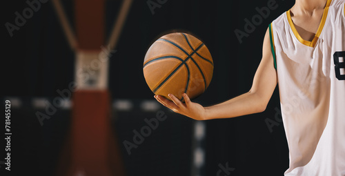 Young basketball player holds classic ball. Basket in background. Junior level basketball player holding game ball. Basketball training session for kids photo