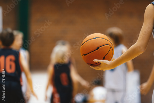 Young basketball player with classic basketball. Basketball training session for kids. Team players in blurred background. Junior level basketball player holding game ball photo