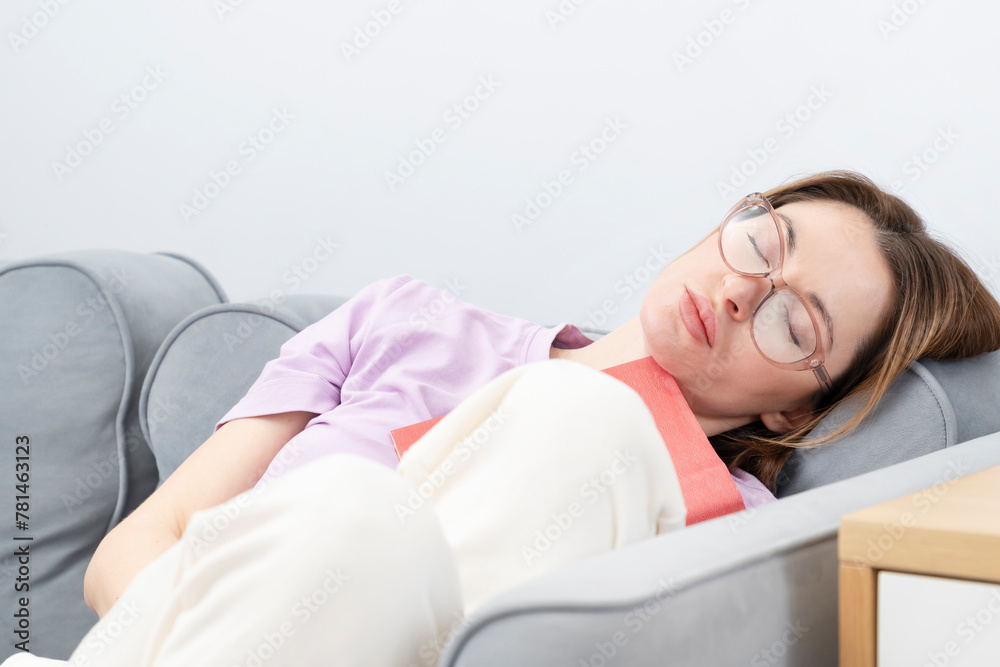 Tired girl sitting on the couch with book on her face sleeping during education	
