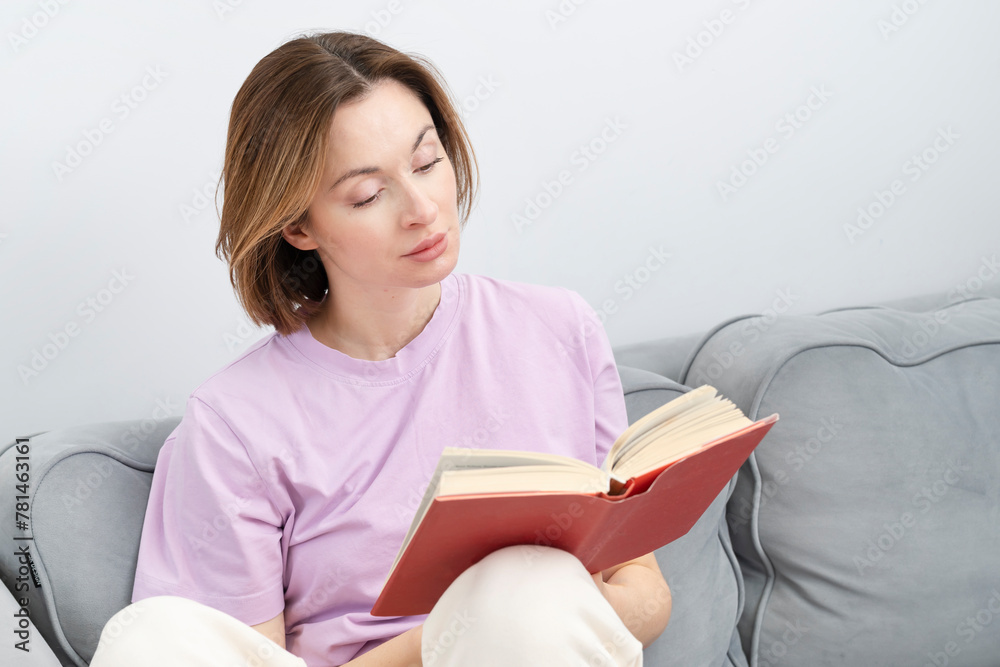 Young attractive woman sits on the couch and reads a book. Home education and leisure time concept Young attractive woman sits on the couch and reads a book. Home education and leisure time concept