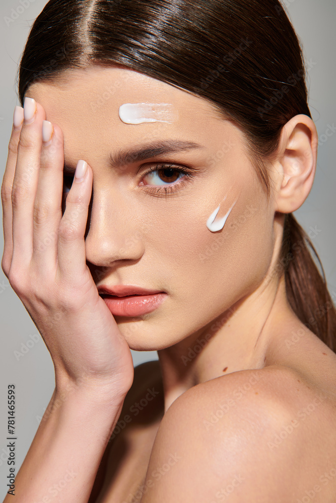 A young woman with brunette hair poses in a studio setting, delicately holding her hand up to her face in a contemplative gesture.