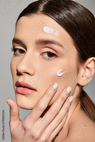 A young woman with brunette hair posing in a studio environment  with a generous amount of cream on her face.