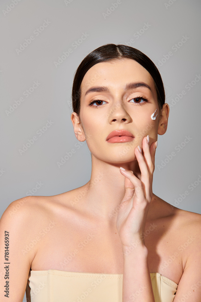 Brunette woman oozes elegance in a strapless dress, striking a pose with her hand delicately touching her face. Brunette woman oozes elegance in a strapless dress, striking a pose with her hand delicately touching her face.