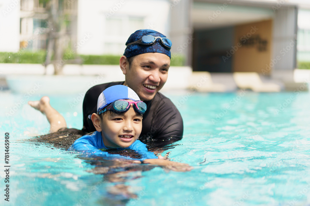 Little boy and father enjoy swimming together in swimming pool.