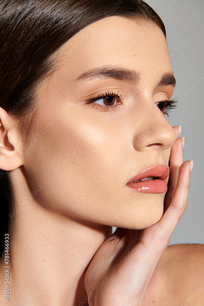 A young woman with brunette hair gracefully places her hand on her face, lost in thought. A young woman with brunette hair gracefully places her hand on her face, lost in thought.