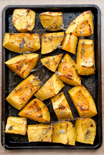 Pieces of organic oven roasted butternut squash in a baking sheet pan with fresh thyme and sage herbs in natural light.