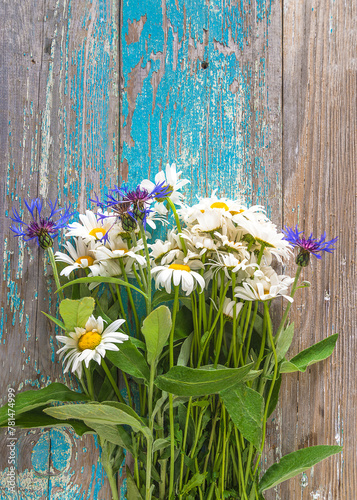 Mother's day greeting card; bunch of white daisies and cornflowers on a old blue paint wooden background; copy space