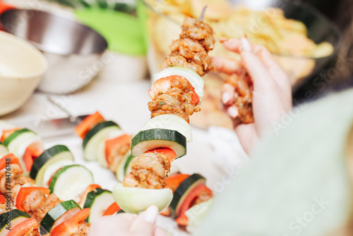 Shashlik cuisine. Metal sticks with vegetable and meat. Raw chicken, onion and bell pepper slices. Grilling food on a picnic. Girl in kitchen. Woman hands preparing dinner.