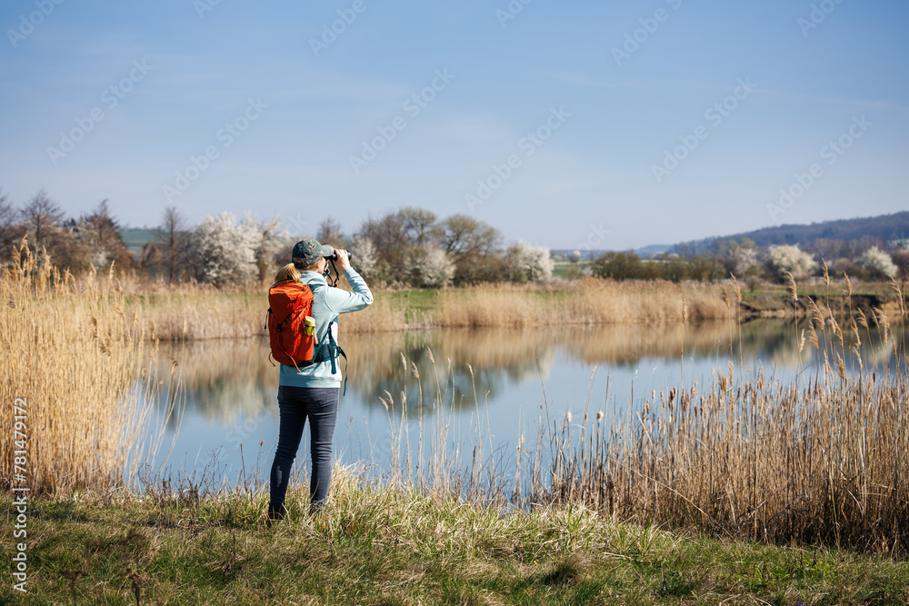 Eco tourism. Woman hiker with binoculars watching birds and wildlife animals at lake. Hiking and bird watching in spring nature