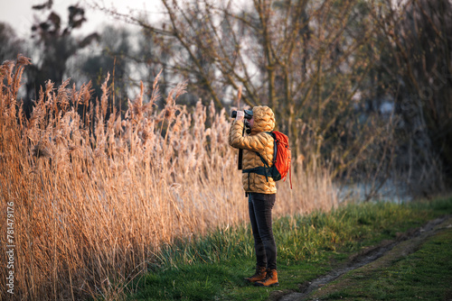 Woman naturalist is watching birds with binoculars. Hiking and wildlife observation at lake © encierro