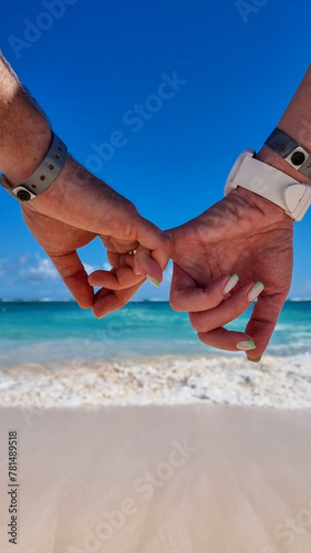 dwoje ludzi na plaży trzyma się za ręce, w oddali morze, słońce, fale photo