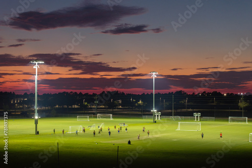 Illuminated public sports arena in North Port, Florida with people playing soccer game on grass football stadium at sunset. Outdoor activities concept © bilanol