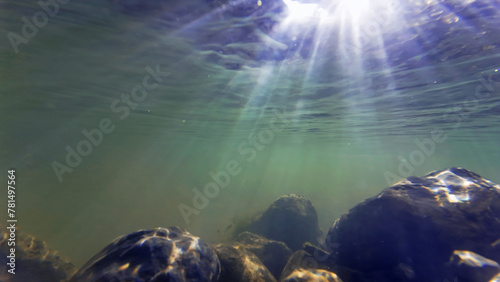 Unterwasseraufnahme vom Grund eines Flusses in dem die Lichtstrahlen der Sonne in Wasser fallen