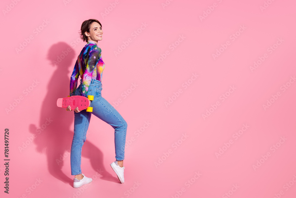 Full size rear photo of nice young woman hold skate look empty space wear pullover isolated on pink color background Full size rear photo of nice young woman hold skate look empty space wear pullover isolated on pink color background