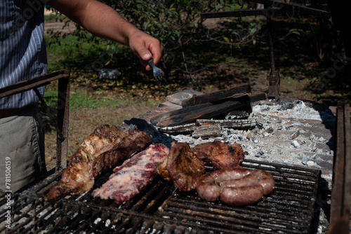 Mano con tenedor y asado de carne vacuna en primer plano, sobre parilla, aire libre, tradicional Argentina photo
