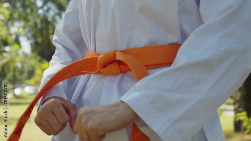 Tilt down shot of Asian female athlete tying up orange belt while practicing taekwondo outdoors