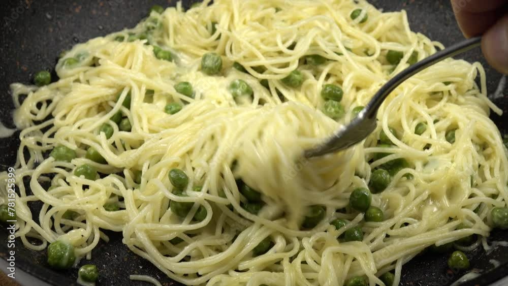 Traditional twirling on a fork italian spaghetti with green peas and grated cheese on a frying pan to make it easier to place them on a plate Traditional twirling on a fork italian spaghetti with green peas and grated cheese on a frying pan to make it easier to place them on a plate