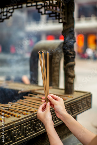 Hands of a woman holding burning incense sticks in the Jing'an temple in Shanghai