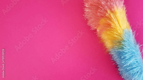 Multicolored brush sweeps dust off pink surface. Concept of cleaning, cleanliness, hygiene. Place to insert text, advertising, message, design. Pipidastra slowly slides along the wall photo